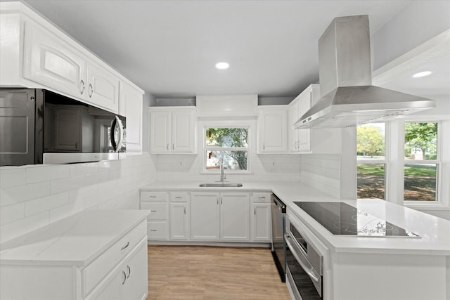 kitchen featuring backsplash, light wood-style flooring, island range hood, stainless steel appliances, and a sink