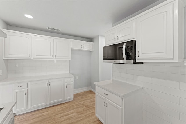 kitchen featuring visible vents, light wood-style flooring, light countertops, white cabinets, and backsplash