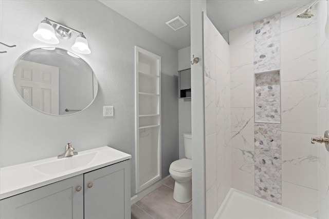 bathroom with visible vents, toilet, a tile shower, tile patterned floors, and vanity