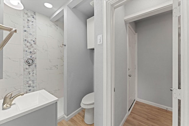 bathroom with toilet, wood finished floors, baseboards, and walk in shower