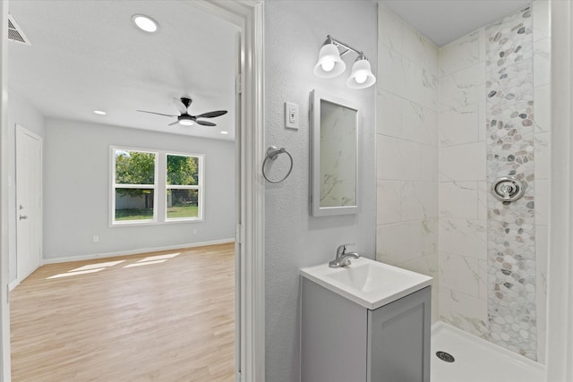 full bathroom with baseboards, tiled shower, wood finished floors, vanity, and a ceiling fan