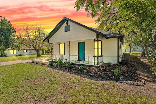 bungalow-style house featuring a porch, a yard, central AC, and a shingled roof