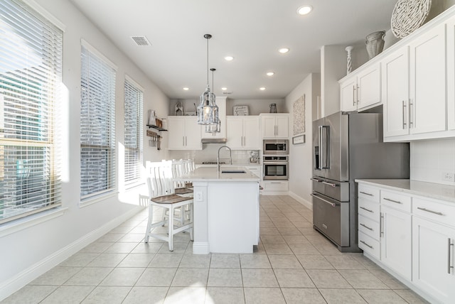 kitchen featuring an island with sink, decorative light fixtures, appliances with stainless steel finishes, and white cabinets