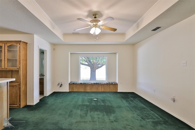 spare room featuring dark colored carpet, ceiling fan, ornamental molding, and a tray ceiling