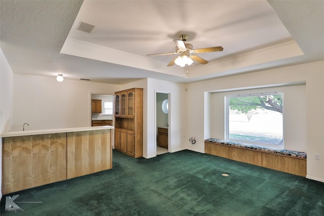 interior space featuring a tray ceiling, kitchen peninsula, ceiling fan, and dark colored carpet