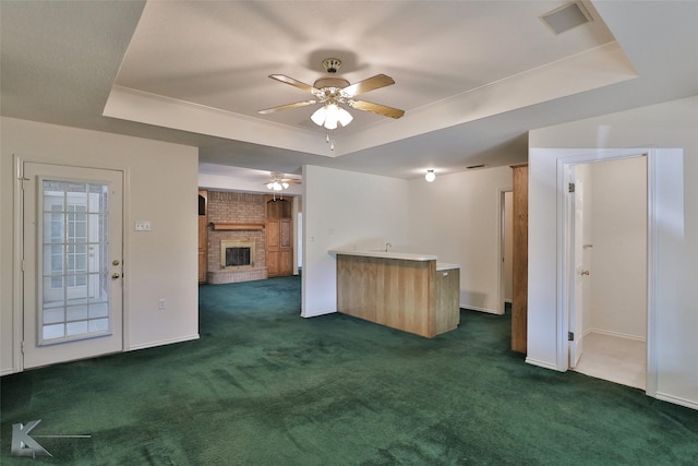 unfurnished living room featuring dark colored carpet, a brick fireplace, and a raised ceiling