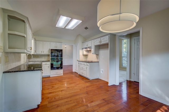 kitchen featuring lofted ceiling, under cabinet range hood, wood finished floors, a sink, and black appliances