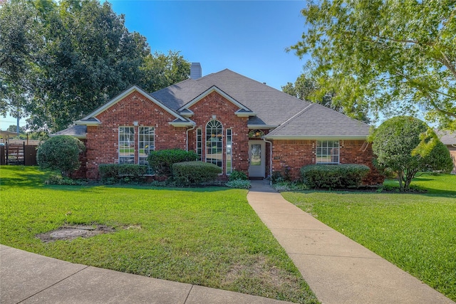 traditional home with brick siding, a chimney, a front yard, and a shingled roof