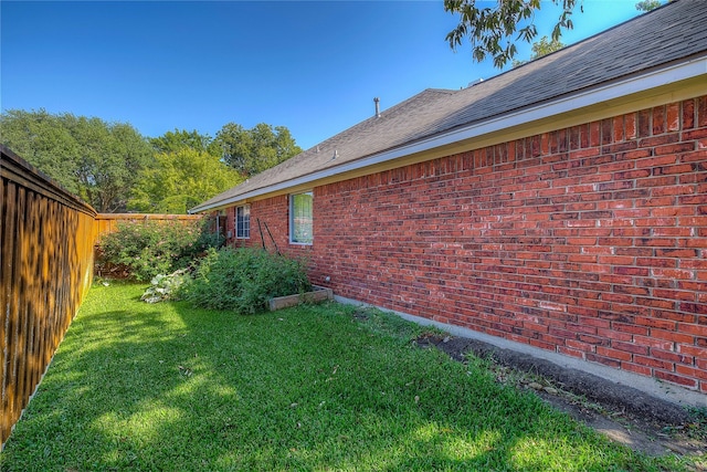 view of home's exterior with roof with shingles, brick siding, fence, and a lawn