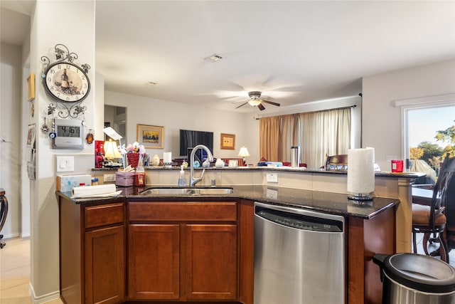 kitchen with sink, light tile patterned floors, ceiling fan, stainless steel dishwasher, and dark stone countertops