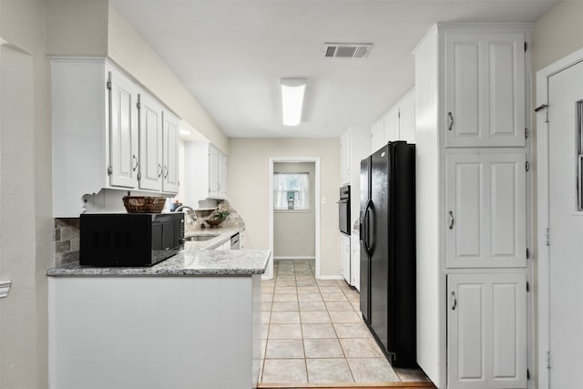 kitchen featuring light stone counters, black appliances, sink, white cabinetry, and light tile patterned floors