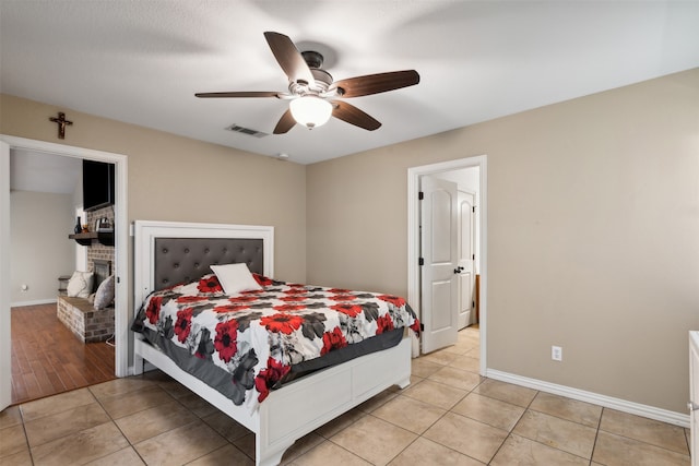 bedroom with light wood-type flooring, ceiling fan, and a brick fireplace