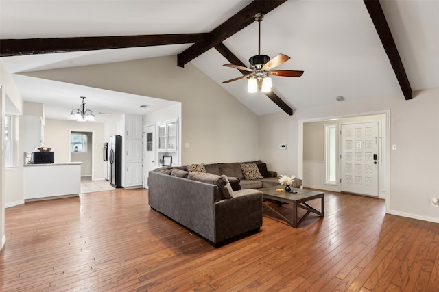 living room featuring ceiling fan with notable chandelier, light hardwood / wood-style flooring, and lofted ceiling with beams