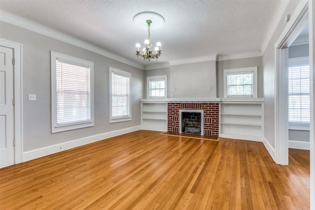 unfurnished living room with a brick fireplace, a textured ceiling, crown molding, wood-type flooring, and a chandelier