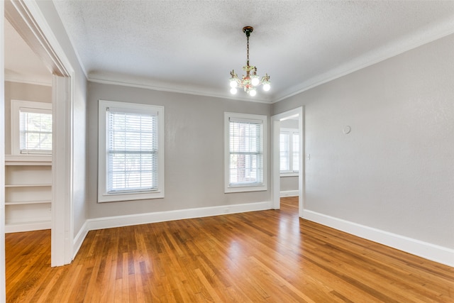 unfurnished room featuring hardwood / wood-style floors, a notable chandelier, ornamental molding, and a textured ceiling