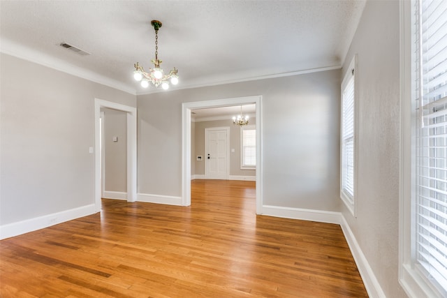 unfurnished room featuring hardwood / wood-style floors, a chandelier, a textured ceiling, and ornamental molding