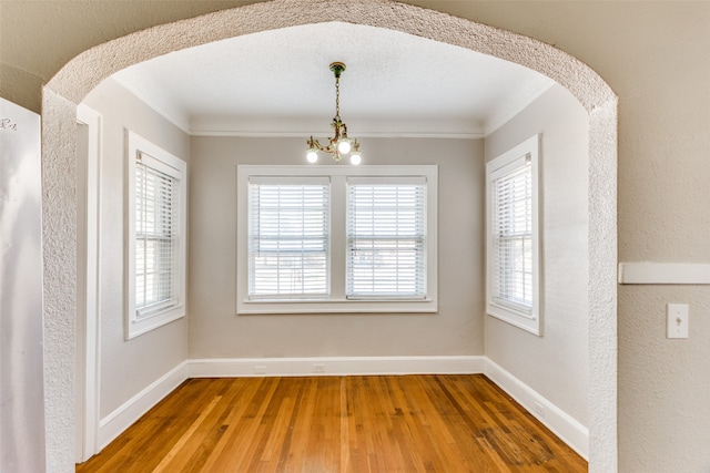 unfurnished dining area with hardwood / wood-style flooring, an inviting chandelier, and ornamental molding