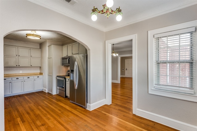 kitchen featuring wood counters, an inviting chandelier, light hardwood / wood-style flooring, crown molding, and appliances with stainless steel finishes