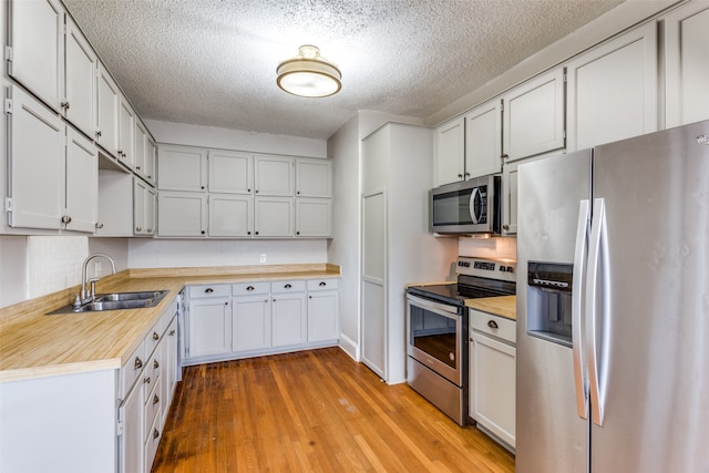 kitchen with white cabinets, sink, appliances with stainless steel finishes, tasteful backsplash, and light hardwood / wood-style floors