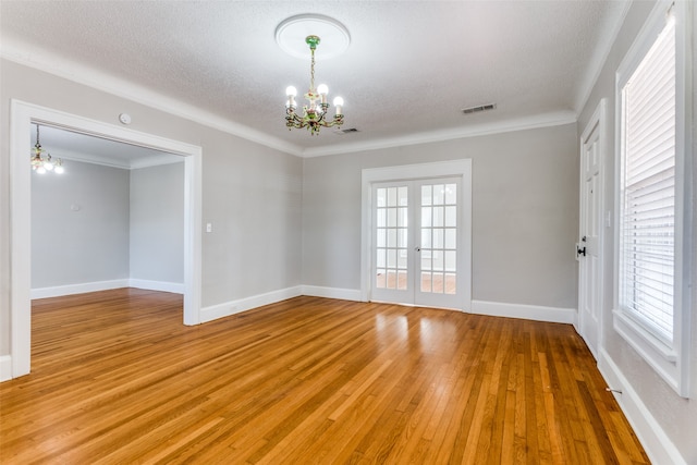 unfurnished room featuring french doors, a notable chandelier, crown molding, a textured ceiling, and hardwood / wood-style flooring