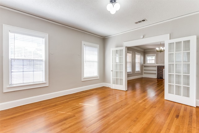 spare room featuring hardwood / wood-style floors, plenty of natural light, french doors, and a notable chandelier