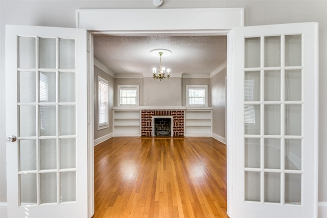 unfurnished living room with an inviting chandelier, a brick fireplace, ornamental molding, a textured ceiling, and wood-type flooring