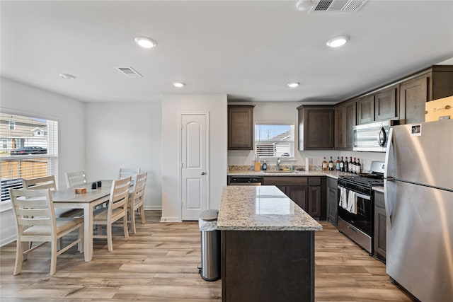 kitchen with light wood-type flooring, a kitchen island, light stone counters, sink, and appliances with stainless steel finishes