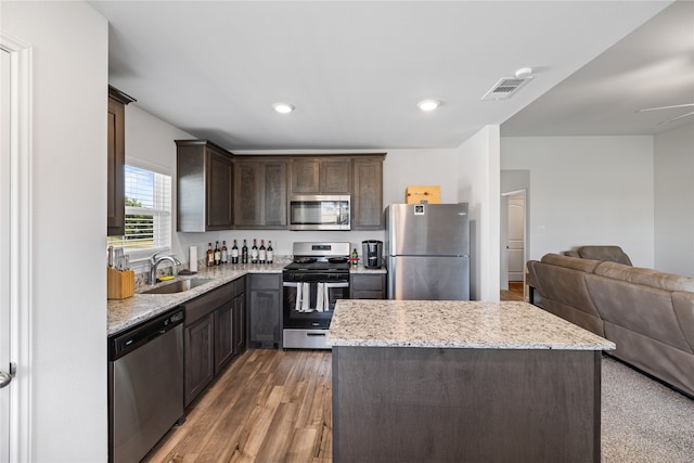 kitchen with a kitchen island, dark wood-type flooring, sink, light stone countertops, and appliances with stainless steel finishes