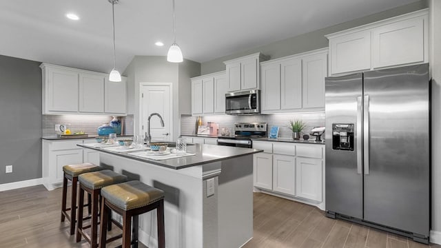 kitchen with a center island with sink, appliances with stainless steel finishes, tasteful backsplash, decorative light fixtures, and white cabinetry