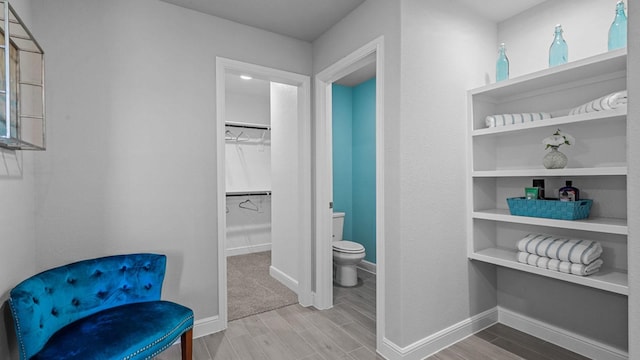 bathroom with toilet, wood finished floors, baseboards, and a spacious closet