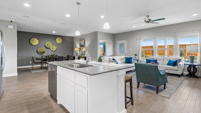 kitchen featuring sink, pendant lighting, light hardwood / wood-style floors, a center island with sink, and white cabinets