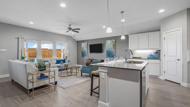 kitchen with sink, decorative light fixtures, a center island with sink, light hardwood / wood-style floors, and white cabinetry