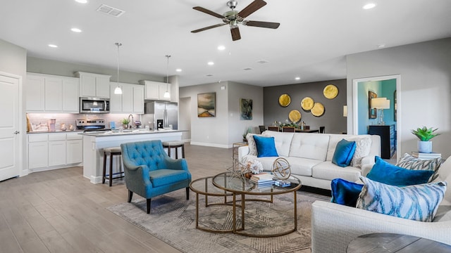 living room featuring ceiling fan, sink, and light wood-type flooring