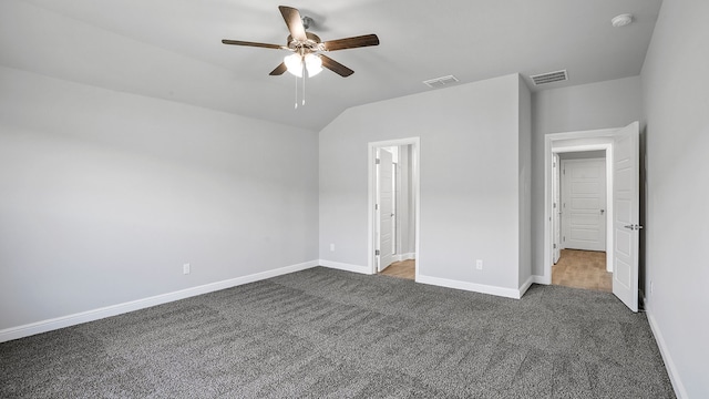 unfurnished bedroom featuring lofted ceiling, dark colored carpet, ensuite bathroom, and ceiling fan