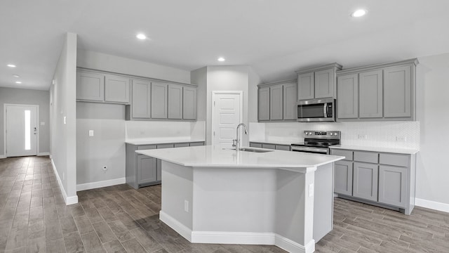 kitchen with appliances with stainless steel finishes, a kitchen island with sink, sink, and light hardwood / wood-style floors