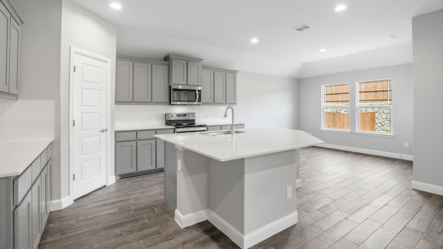 kitchen with a kitchen island with sink, dark hardwood / wood-style floors, stainless steel appliances, gray cabinetry, and sink