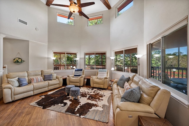 living room with a wealth of natural light, wood-type flooring, a towering ceiling, and ceiling fan