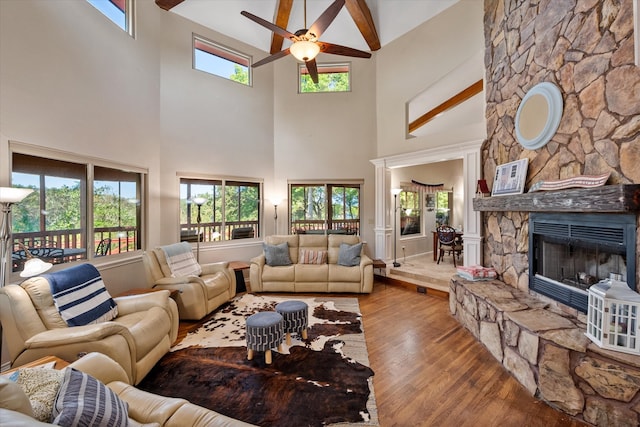 living room with a stone fireplace, hardwood / wood-style flooring, beamed ceiling, and high vaulted ceiling