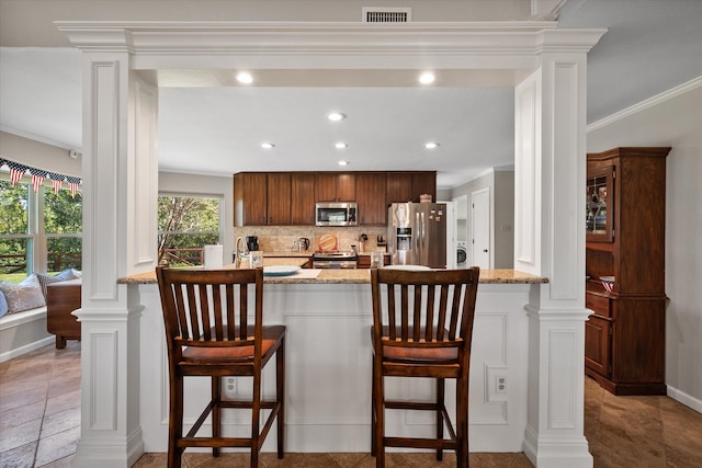 kitchen featuring a breakfast bar area, decorative backsplash, light stone counters, and stainless steel appliances