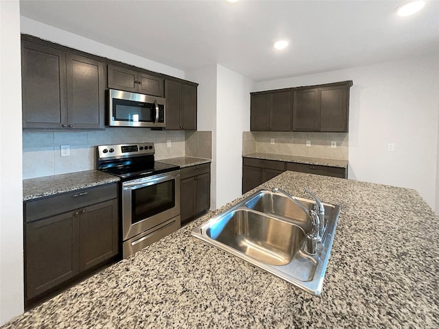 kitchen featuring light stone counters, dark brown cabinetry, stainless steel appliances, tasteful backsplash, and sink