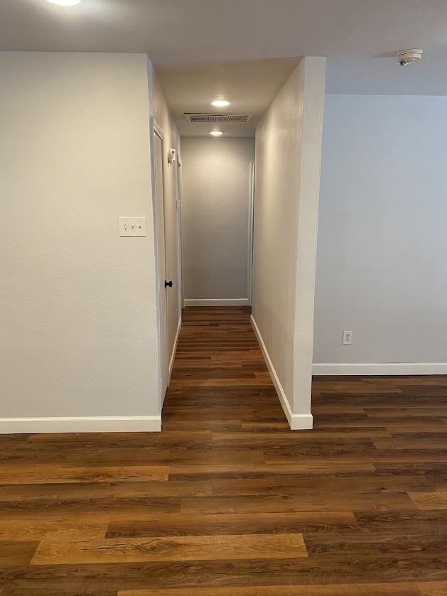 hallway featuring dark wood finished floors, visible vents, and baseboards