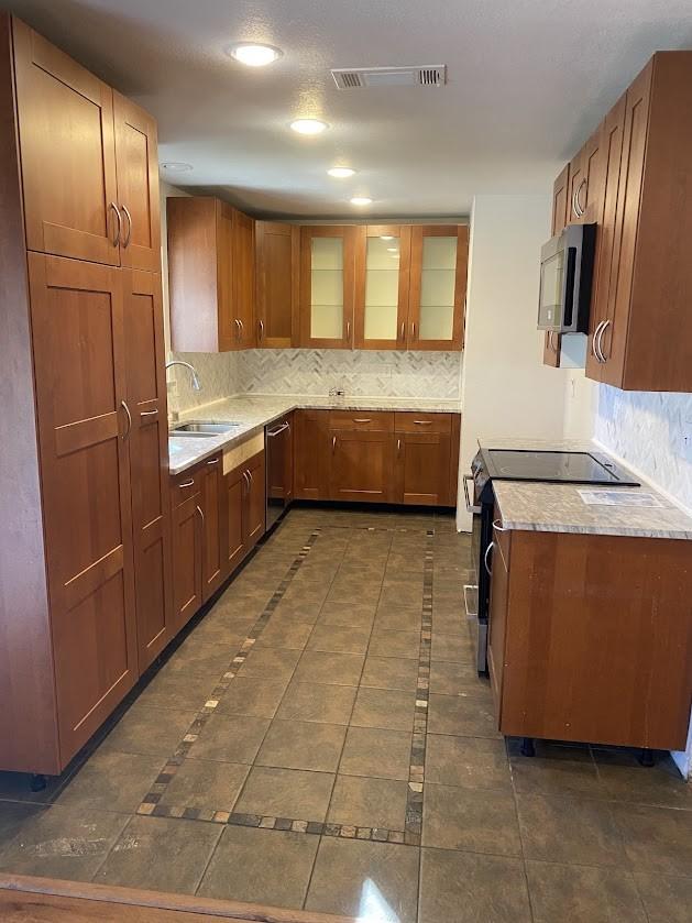 kitchen with stainless steel appliances, a sink, visible vents, tasteful backsplash, and glass insert cabinets