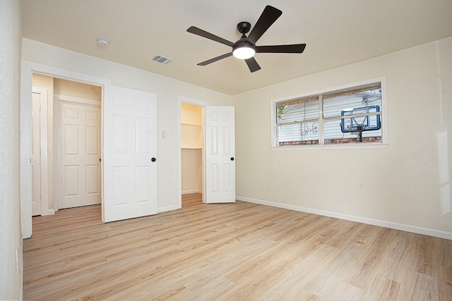 unfurnished bedroom with a walk in closet, light hardwood / wood-style flooring, a closet, and ceiling fan