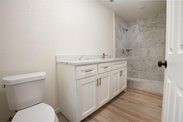 bathroom featuring hardwood / wood-style flooring, tiled shower, vanity, and toilet