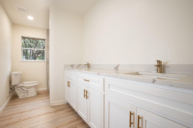 bathroom featuring toilet, wood finished floors, visible vents, a sink, and baseboards