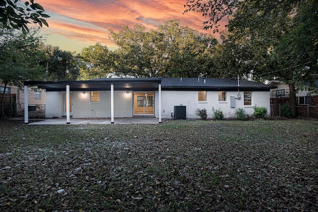 back house at dusk featuring central AC, a yard, and a patio