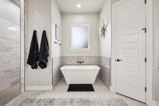 bathroom featuring walk in shower, a freestanding tub, tile walls, and tile patterned floors