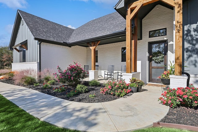 property entrance with brick siding, covered porch, board and batten siding, and roof with shingles