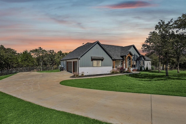 modern farmhouse with a shingled roof, concrete driveway, fence, board and batten siding, and a front yard