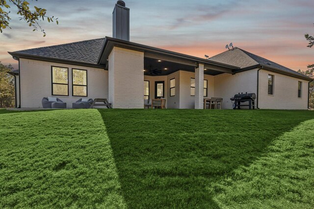 rear view of property with ceiling fan, a chimney, a lawn, and brick siding